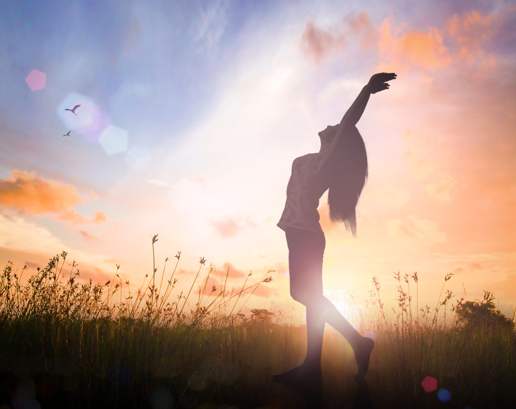 World environment day concept: Silhouette of healthy woman raised hands for praise and worship God at sunset meadow background.